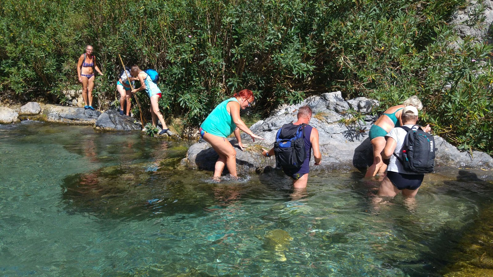 Group crossing a clear green pool on the Kourtaliotiko Gorge river route